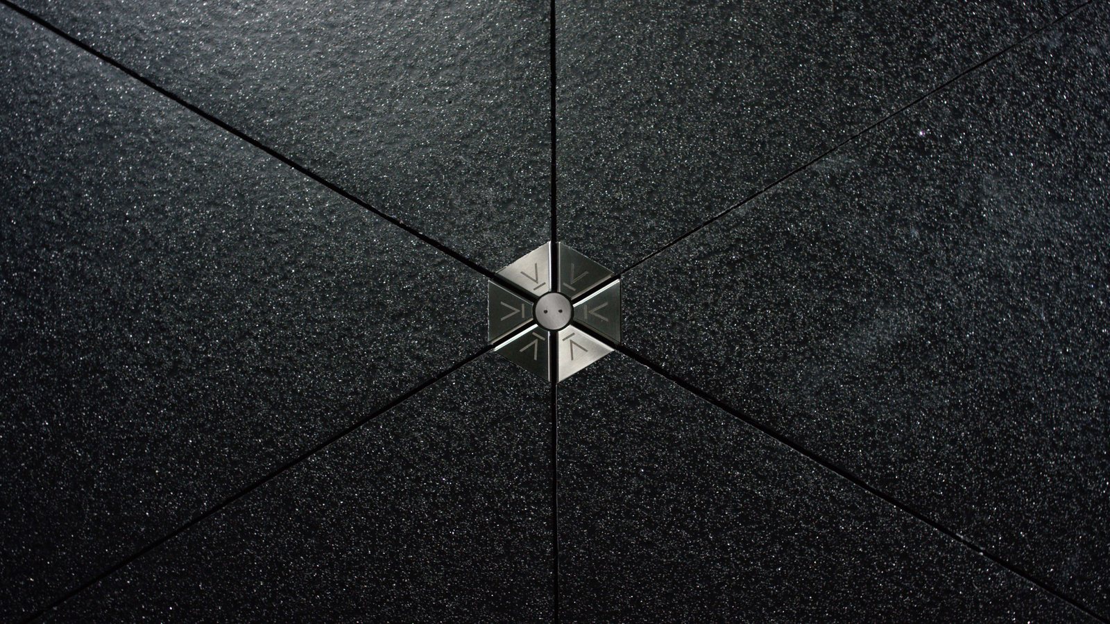 Close-up of a dark Pavegen floor tile, triangular panels meeting at a metal hub in the centre.