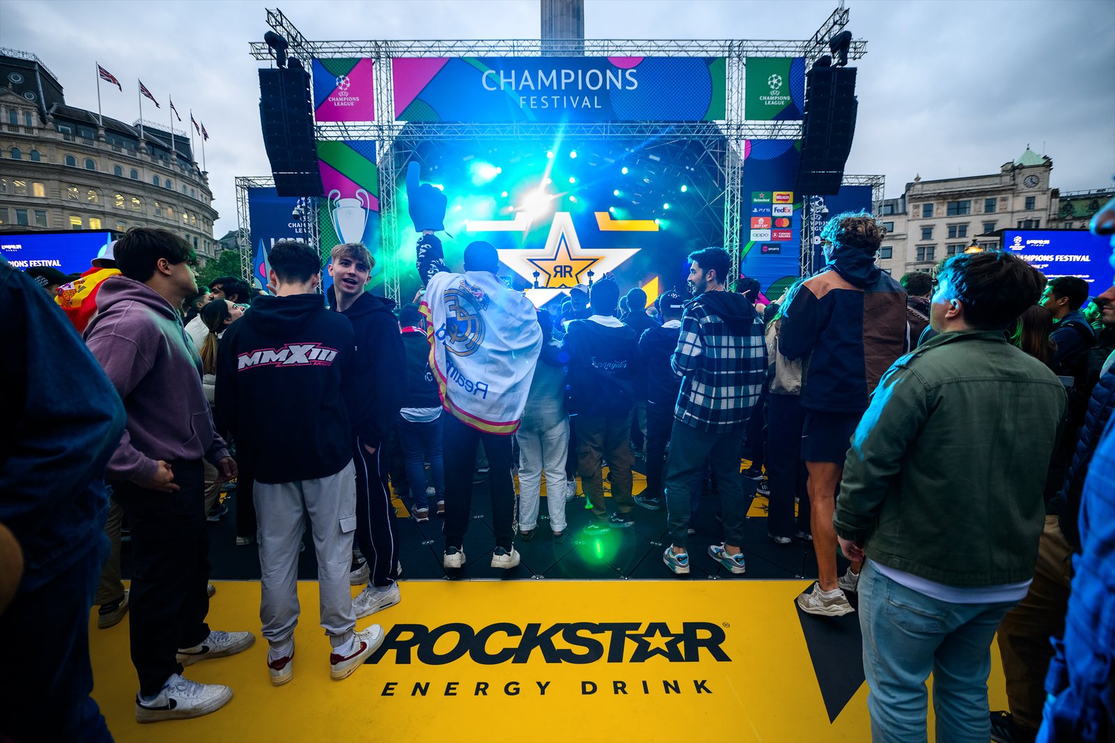 A crowd facing the Champions Festival stage in Trafalgar Square, standing on a yellow Rockstar Energy Drink floor.