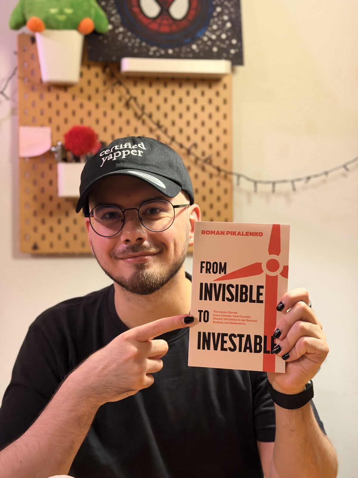 Roman Pikalenko holding a paperback copy of From Invisible to Investable and pointing at it.